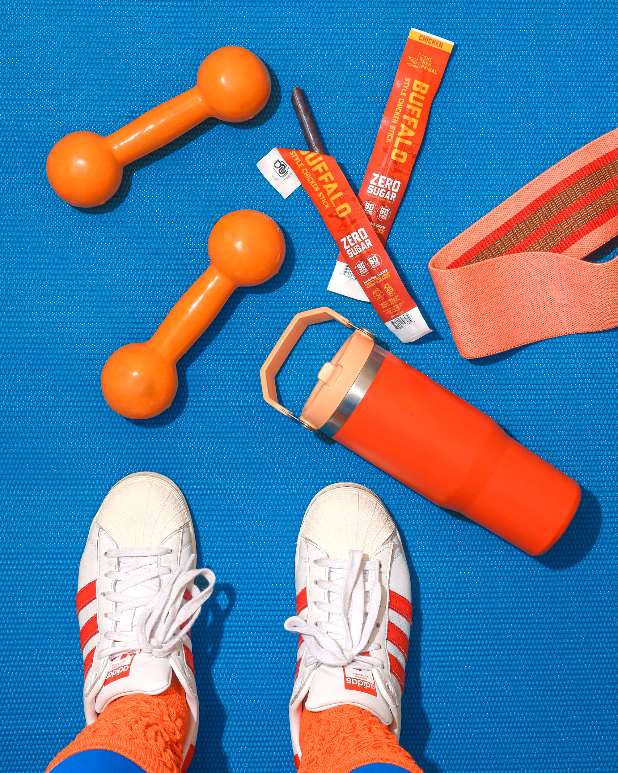 blue mat with orange buffalo chicken stick and orange stanley cup with white stan smiths on the bottom of the image