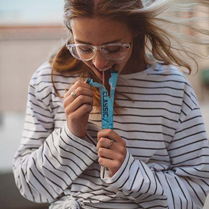 a woman in clear glasses and a blue and white nautical striped sweater holding a classic beef stick in her hand and taking a bite.