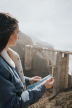 a woman in a denim jacket holding a classic beef stick looking off into the distance in a mountain region